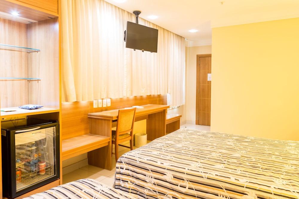 Hotel Atlantico Business Centro Rio de Janeiro Buitenkant foto The photo shows a hotel room with two beds featuring striped bedding. There is a wooden desk and chair near a window with light-colored curtains. A flat-screen television is mounted on the wall, and there appears to be a small refrigerator or mini-ba
