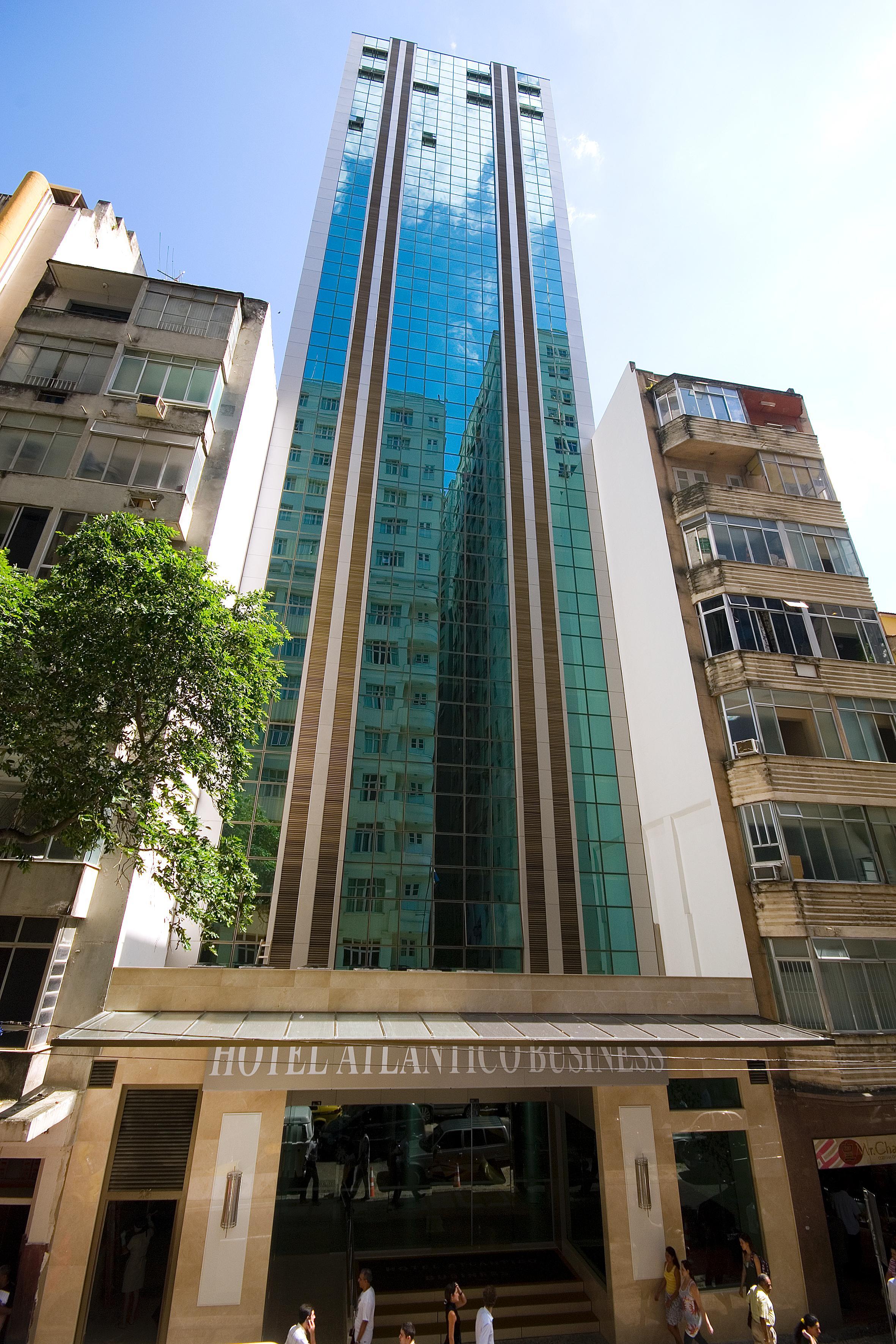Hotel Atlantico Business Centro Rio de Janeiro Buitenkant foto The photo shows a modern multi-story building with a sleek glass facade. The building appears to have several floors with large windows, reflecting sunlight, and is flanked by a tree on one side and an older, more traditional residential structure on